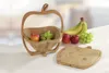 A wooden apple-shaped fruit basket with fruit inside and a matching cutting board next to it. Podgląd zdjęcia produktu