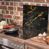A kitchen scene with a glass hob cover featuring a black and gold marble design, a frying pan, vegetables, and cooking utensils on a stovetop. Náhľad obrázku produktu
