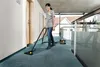 A woman is vacuuming a hallway with a Karcher industrial vacuum cleaner. Produktbild-Vorschau