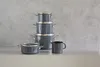 A set of dark gray pots and a mug are displayed on a white surface against a textured gray background. Anteprima dell’immagine prodotto