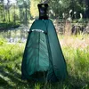 A portable shower tent set up outdoors by a body of water, with a water bag hanging from a tree branch above it. Náhled obrázku produktu