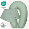 A pale green U-shaped maternity pillow with a removable cover. The pillow is partially covered by its own folded cover, secured with a wooden toggle and loop. Text overlays include an OEKO-TEX Standard 100 logo and German text describing the product. Produktbild-Vorschau