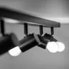 Close-up of a black ceiling light fixture with four adjustable spotlights, showing two of the bulbs illuminated. Voir les images du produit