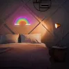 A bedroom scene with a bed, pillows, a blanket, a neon rainbow light, and a desk lamp. Produktbild-Vorschau