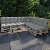 An outdoor seating area with a modular sofa made of pallets and cushions, a coffee table, and a rug, surrounded by greenery. Anteprima dell’immagine prodotto