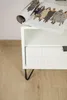 A close-up of a white nightstand with a magazine on top and a black hairpin leg. Podgląd zdjęcia produktu