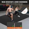 Two people are exercising on a large black mat in a gym setting. The mat is the focus of the image, with text highlighting its features. Voir les images du produit