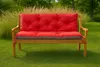A red and gray tufted cushion set on a wooden garden bench, placed on a green lawn with tall grasses and trees in the background. Produktbild-Vorschau
