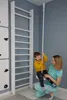 A woman is holding a child on a rope swing next to a wooden ladder in a room. Voir les images du produit