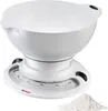A white kitchen scale with a mixing bowl on top, next to a pile of flour. Náhľad obrázku produktu