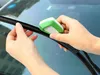 Hands cleaning a car windshield wiper with a small green and white cleaning tool. Produktbild-Vorschau
