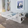 A white wooden children's bed with a built-in shelf unit and a small desk area, set in a child's bedroom with shelves and artwork on the wall. Produktbild-Vorschau
