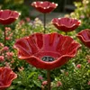 Mehrere rote, blumenförmige Keramik-Vogeltränken auf Stäben, platziert in einer Gartenumgebung mit grünem Laub und kleinen rosa Produktbild-Vorschau