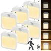 A group of white LED night lights with motion and dusk sensors, illuminated with a warm yellow light, are arranged in a cluster. To the right, a series of smaller images show the lights in different lighting conditions, a silhouette of a person walking, an Produktbild-Vorschau
