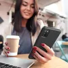 A woman holding a phone and a coffee cup at a table with a laptop. Produktbild-Vorschau
