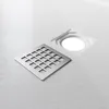A close-up, angled view of a square shower drain grate and the drain opening on a textured white shower tray. Podgląd zdjęcia produktu