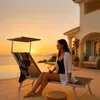 A woman relaxing on a lounge chair by a pool at sunset. Anteprima dell’immagine prodotto