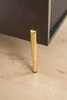 Close-up of a single gold-colored furniture leg attached to a dark-colored cabinet, resting on a light wooden floor. Produktbild-Vorschau
