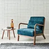 A blue velvet armchair with a wooden frame is placed in a room with a grid-patterned wallpaper and a gray rug. Anteprima dell’immagine prodotto