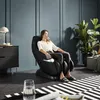 A woman relaxes in a black massage chair in a modern room. Produktbild-Vorschau
