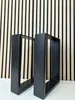 Two black metal table legs are displayed in front of a slatted wood and black panel wall. Náhľad obrázku produktu