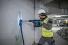 A construction worker is using a rotary hammer drill to drill a hole in a wall in what appears to be a parking garage or industrial building. Produktbild-Vorschau