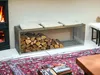 A modern living room with a fireplace and a metal firewood rack filled with logs. Produktbild-Vorschau