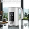 A white electric kettle with a digital display is shown on a kitchen counter, with a blurred background of a window overlooking a landscape. Náhled obrázku produktu