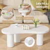 A white cloud-shaped coffee table is shown in a living room setting, with close-up insets demonstrating cleaning and material features. Produktbild-Vorschau