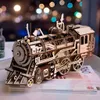 A detailed 3D wooden model of a mechanical steam locomotive is displayed on a stack of books. The background features blurred bokeh lights, suggesting an indoor, possibly evening setting. Náhľad obrázku produktu