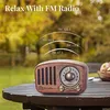 A vintage-style radio sits on a wooden table outdoors, with trees and foliage in the background. Produktbild-Vorschau