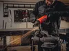 A person is using an angle grinder to cut a metal piece held in a vise in a workshop. Podgląd zdjęcia produktu