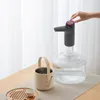 A hand pressing a button on a water dispenser pump that is attached to a large water bottle. Water is flowing from the pump into a small teapot. A tea tray with a cup is also visible. Produktbild-Vorschau