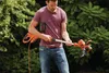 A man is holding a string trimmer in a garden. Produktbild-Vorschau