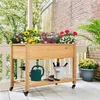 A wooden raised garden bed filled with colorful flowers sits on a porch with a brick wall in the background. Podgląd zdjęcia produktu