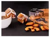 Gingerbread house cookies decorated with white icing, some placed in a white mug of coffee, with cookie dough and a cookie cutter on a dark surface. Produktbild-Vorschau