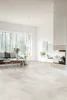 A modern living room with a large window overlooking a forest, featuring a sofa, coffee tables, and a fireplace. Produktbild-Vorschau