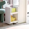 A close-up view of a white storage unit with wheels, featuring two shelves. The top shelf holds a stack of books, one of which is bright yellow. The bottom shelf contains a yellow star-shaped pillow. Anteprima dell’immagine prodotto