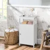 A white bathroom cabinet is shown in a bathroom setting with a woven basket and a wooden stool. Náhled obrázku produktu