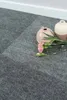 Close-up of gray carpet tiles with two decorative vases and pink flowers. Produktbild-Vorschau