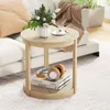A round side table with a vase of flowers and a cup of coffee on top, and books and headphones on the shelf below, placed next to a sofa. Podgląd zdjęcia produktu