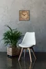 A modern living room setting with a clock, a plant, and a chair. Produktbild-Vorschau