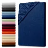 A stack of colorful fitted sheets is shown on the left, and a single navy blue fitted sheet is shown on the right, partially covering a mattress. Produktbild-Vorschau