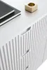 A close-up view of a white dresser with ribbed drawer fronts and a small gold candle holder on top. Produktbild-Vorschau