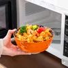 A hand holding a bowl of pasta in front of an open microwave. Náhled obrázku produktu