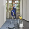 A man is painting a wall with a spray gun while standing on a ladder. A paint sprayer machine is on the floor next to him. Náhľad obrázku produktu