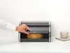 A person's hand is opening a black bread bin with a loaf of bread inside. A mug and napkin are on the right side of the image. Podgląd zdjęcia produktu