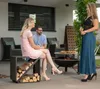People gathered around a fire pit on a patio, with a wood storage unit. Produktbild-Vorschau