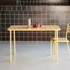 A yellow metal garden table with a red bowl of plums and a silver shaker on it, set against a black tiled wall. Anteprima dell’immagine prodotto