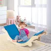 A young child is playing on a wooden rocking climber with a blue cushion in a brightly lit room. Produktbild-Vorschau